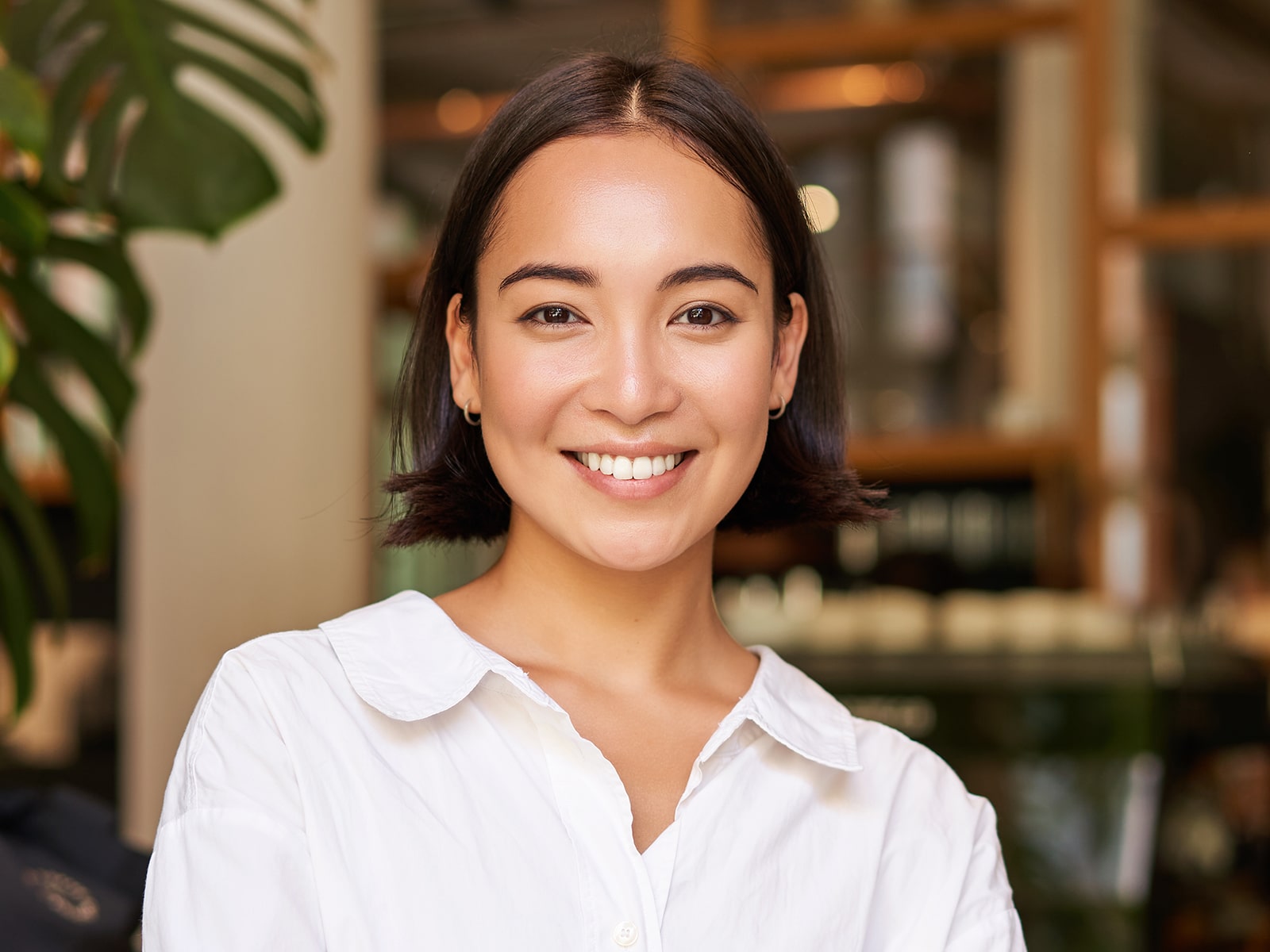 Smiling person with short dark hair wearing a white shirt, standing in a cozy indoor setting.