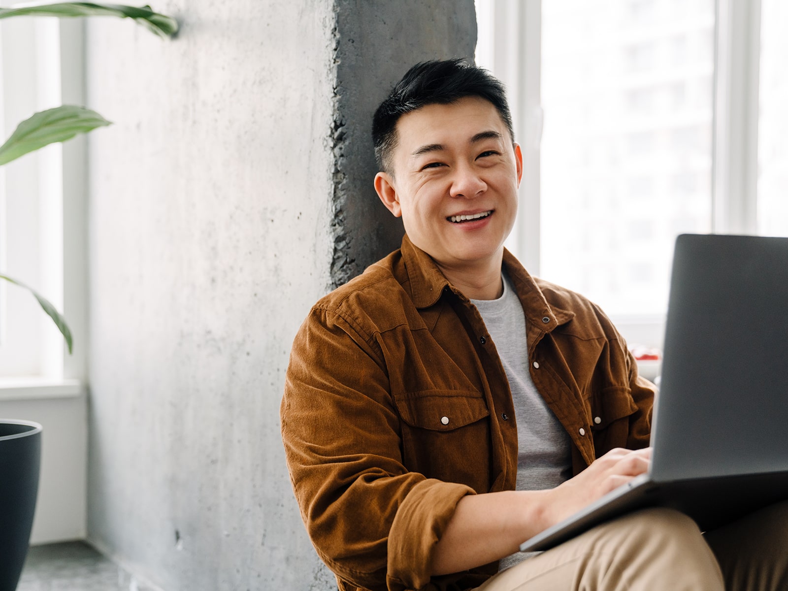 Man smiling with improved teeth while working on a laptop.
